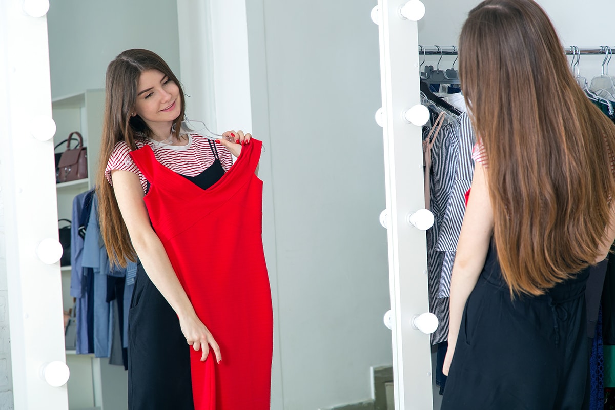 Eine Frau wählt vor dem Spiegel ein rotes, langes Kleid, Farb- und Stilberatung, Personal Shopping